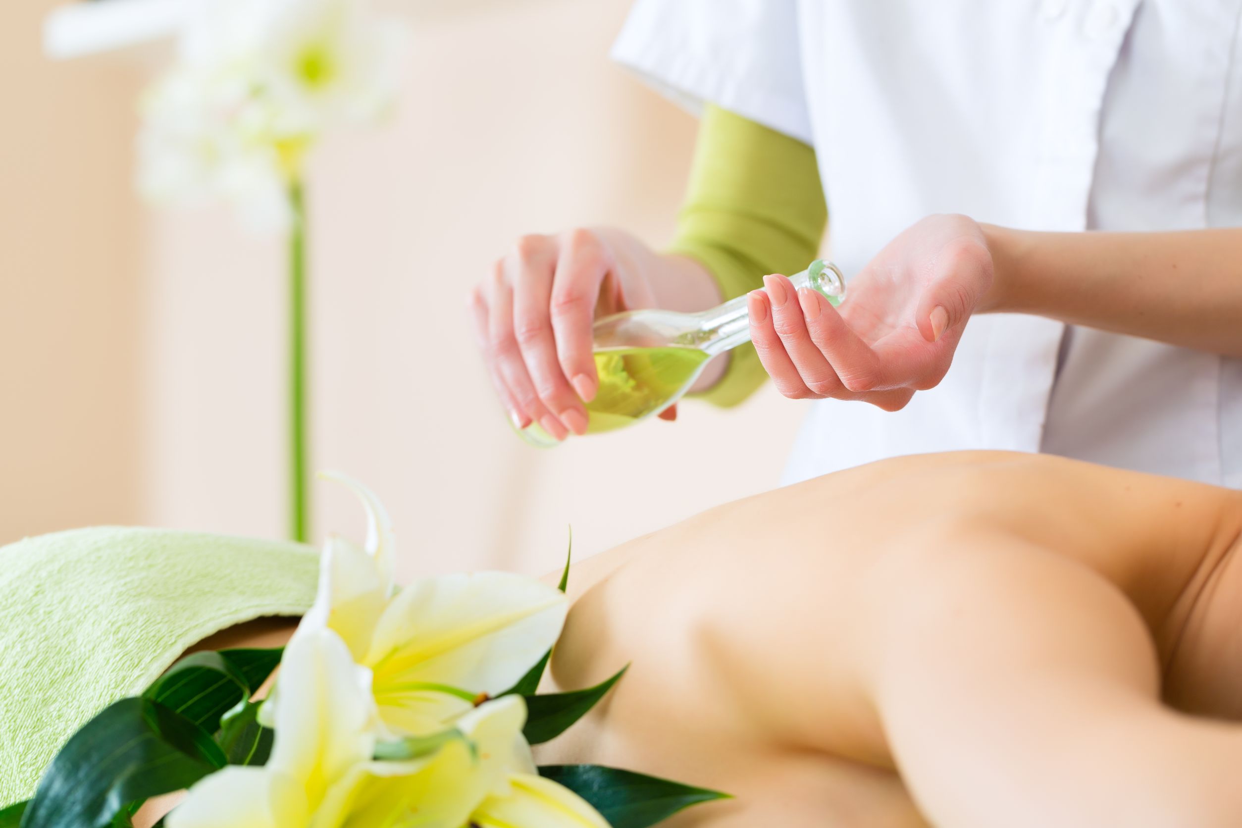 Frau die massiert wird und Masseurin die Öl in die eigenen Hände gibt